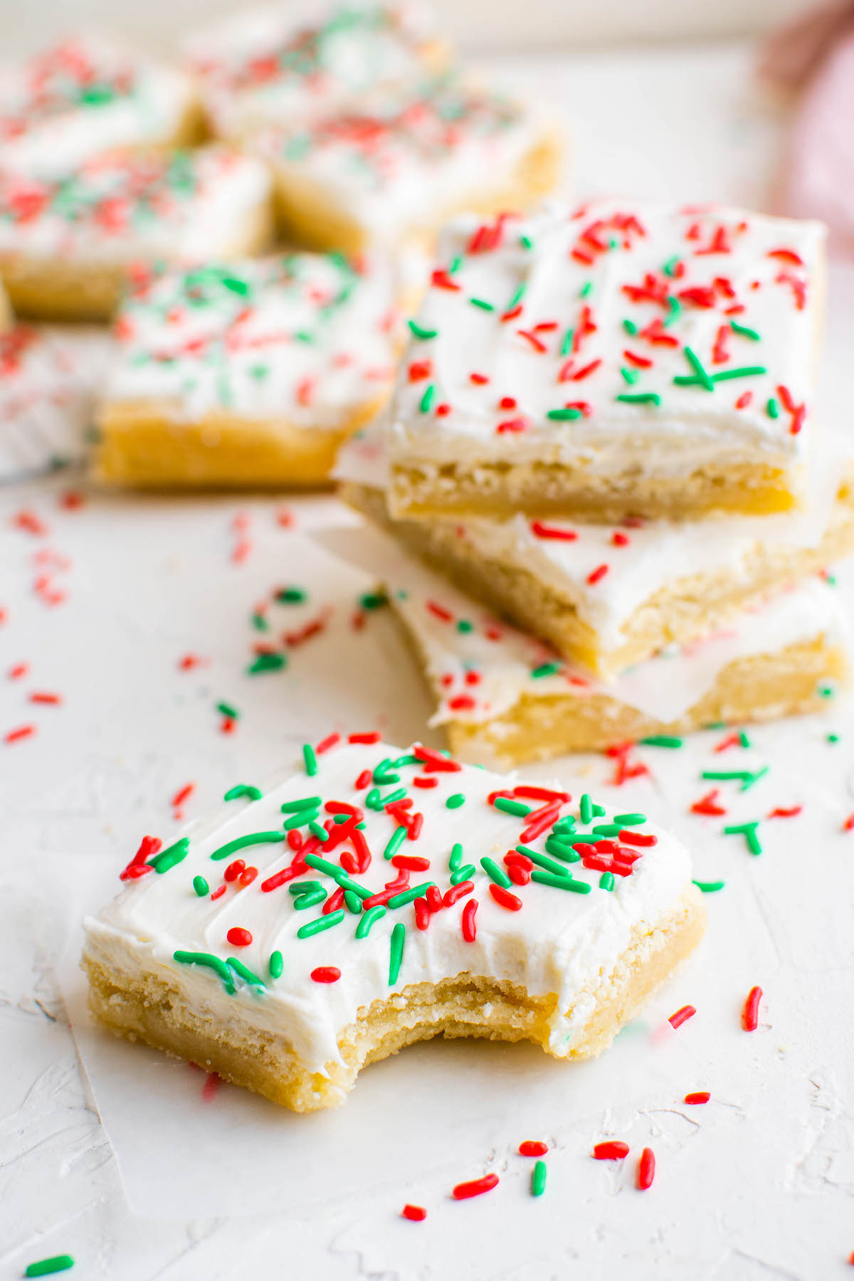 Christmas sugar cookie bars with red and green sprinkles on parchment paper with a bite taken out of one.
