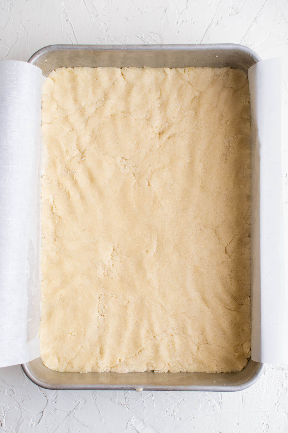 Sugar cookie dough pressed into a baking dish lined with parchment paper.