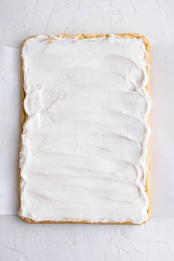 Sugar cookie bars on parchment paper with white frosting spread on top.