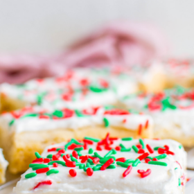 Up close image of a sugar cookie bar with white icing and ready and green sprinkles on top of it on a cookie cooling rack.