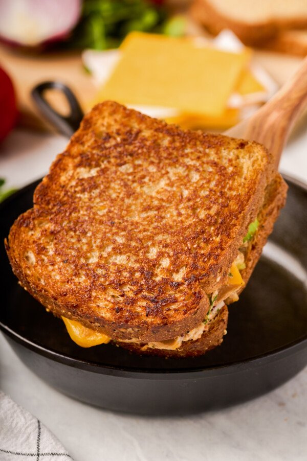 A grilled tuna sandwich is being lifted out of a cast-iron pan with a spatula.