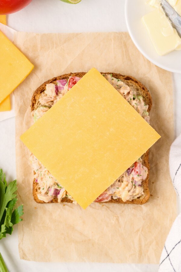 A slice of bread topped with tuna salad and a slice of cheddar cheese.