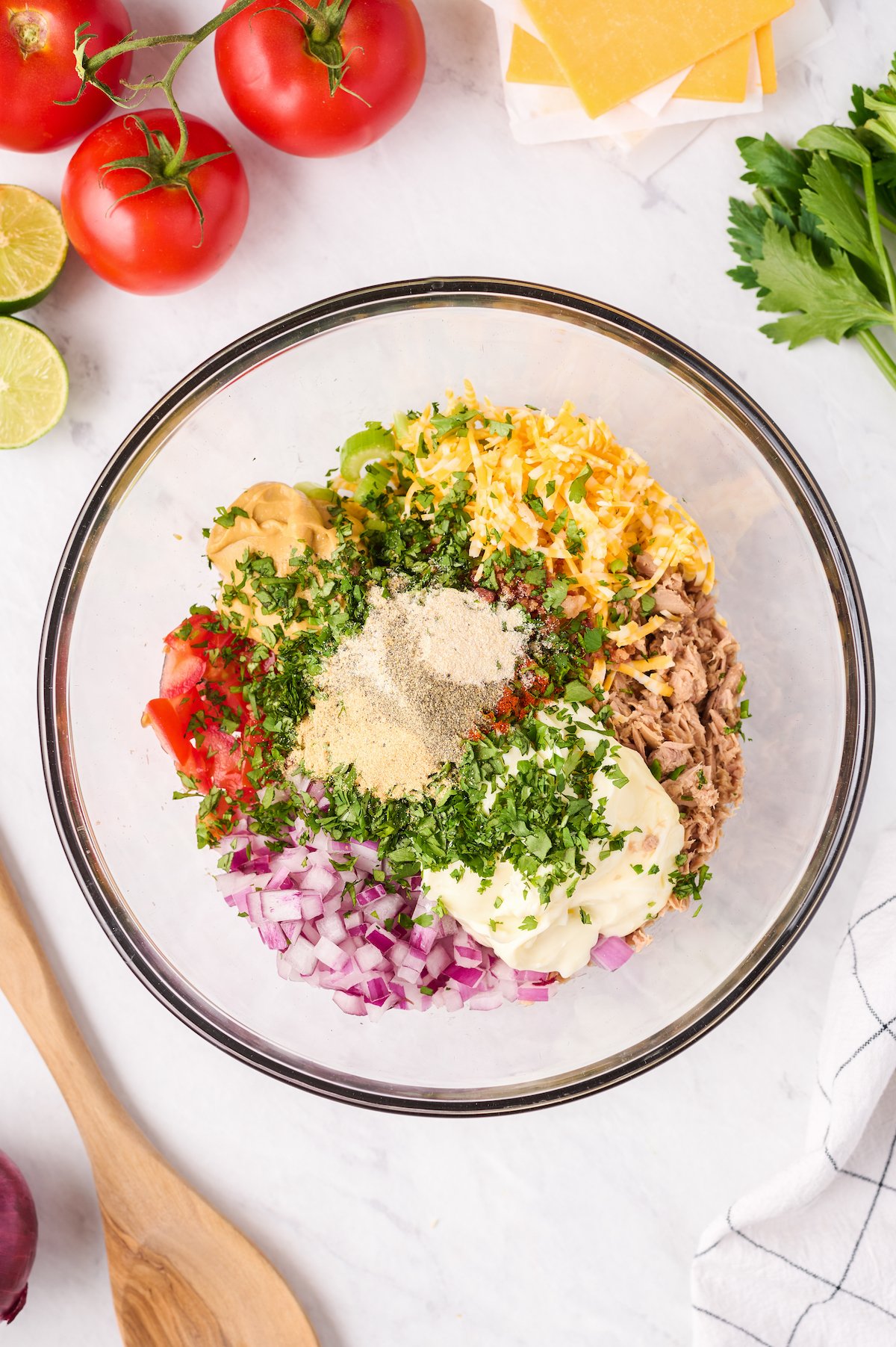 A glass dish with the ingredients for loaded tuna salad arranged inside, and topped with herbs.