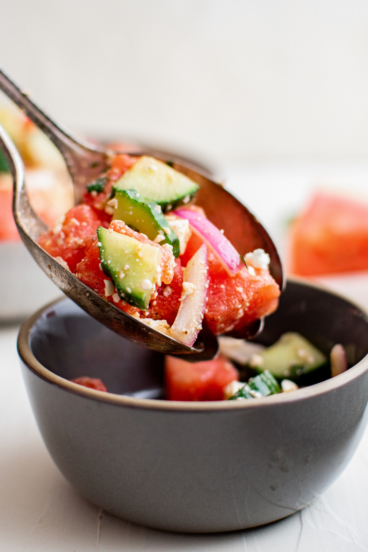 A small salad bowl is being filled with watermelon feta salad.