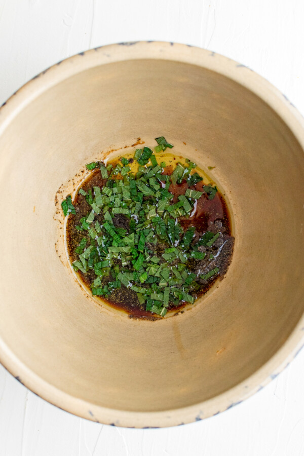 A large salad bowl with oil, balsamic vinegar, mint, and seasonings at the bottom.