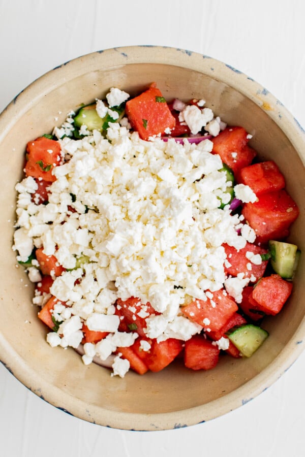A large salad bowl with chopped salad ingredients at the bottom and a generous sprinkling of feta cheese on top.