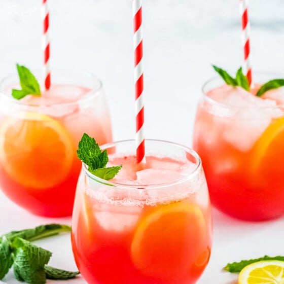 Three glasses of lemonade garnished with mint and paper drinking straws.