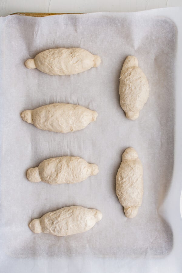 Oval-shaped rolls of unbaked, unrisen dough with knobby ends, on a parchment-lined baking sheet.