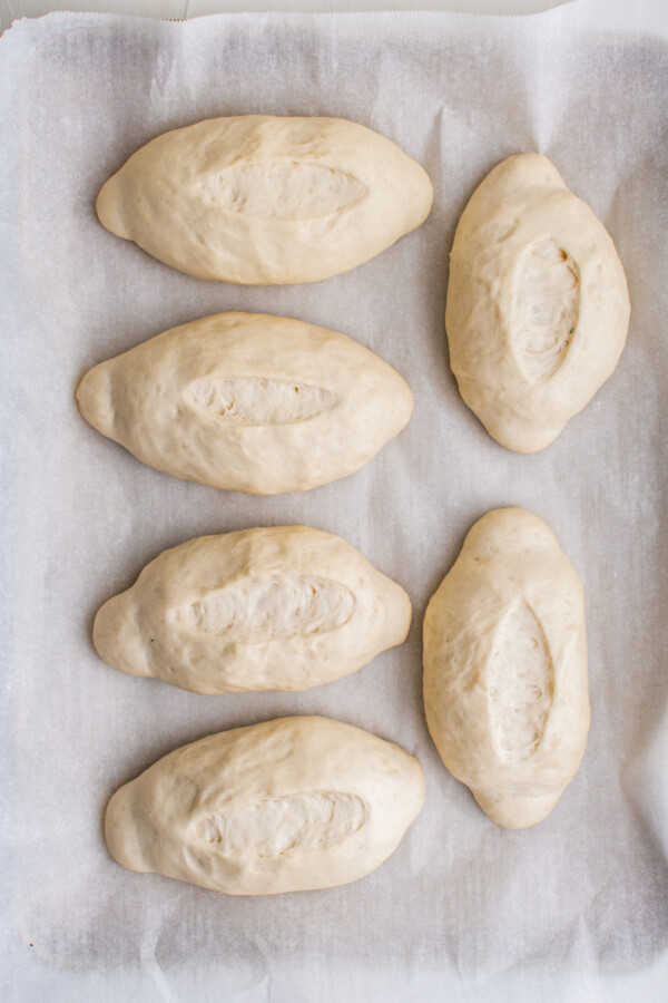Oval-shaped rolls of dough on a parchment-lined baking sheet. The rolls have slashed tops.