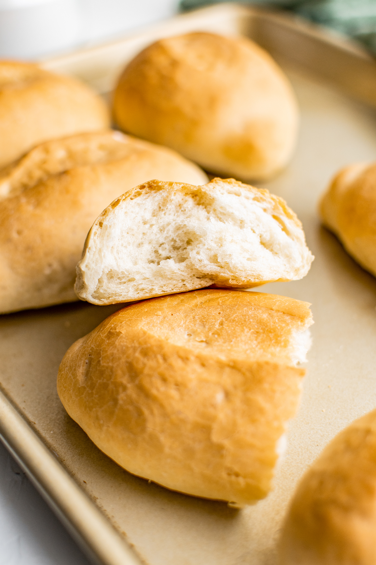 Bread rolls on a baking sheet. One roll has been broken open to show texture.