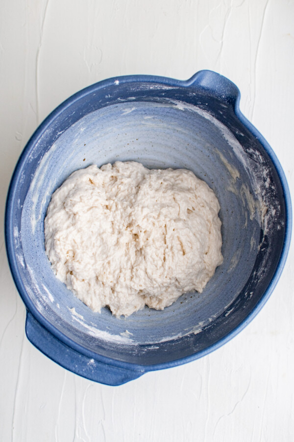 A blue mixing bowl with a rough dough in the bottom.