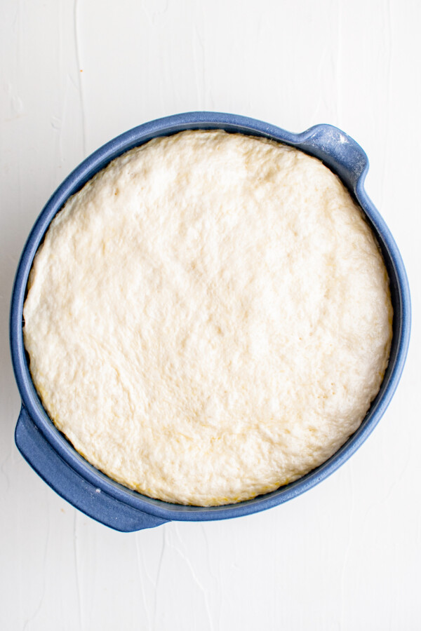 A mixing bowl filled to the top with risen dough.