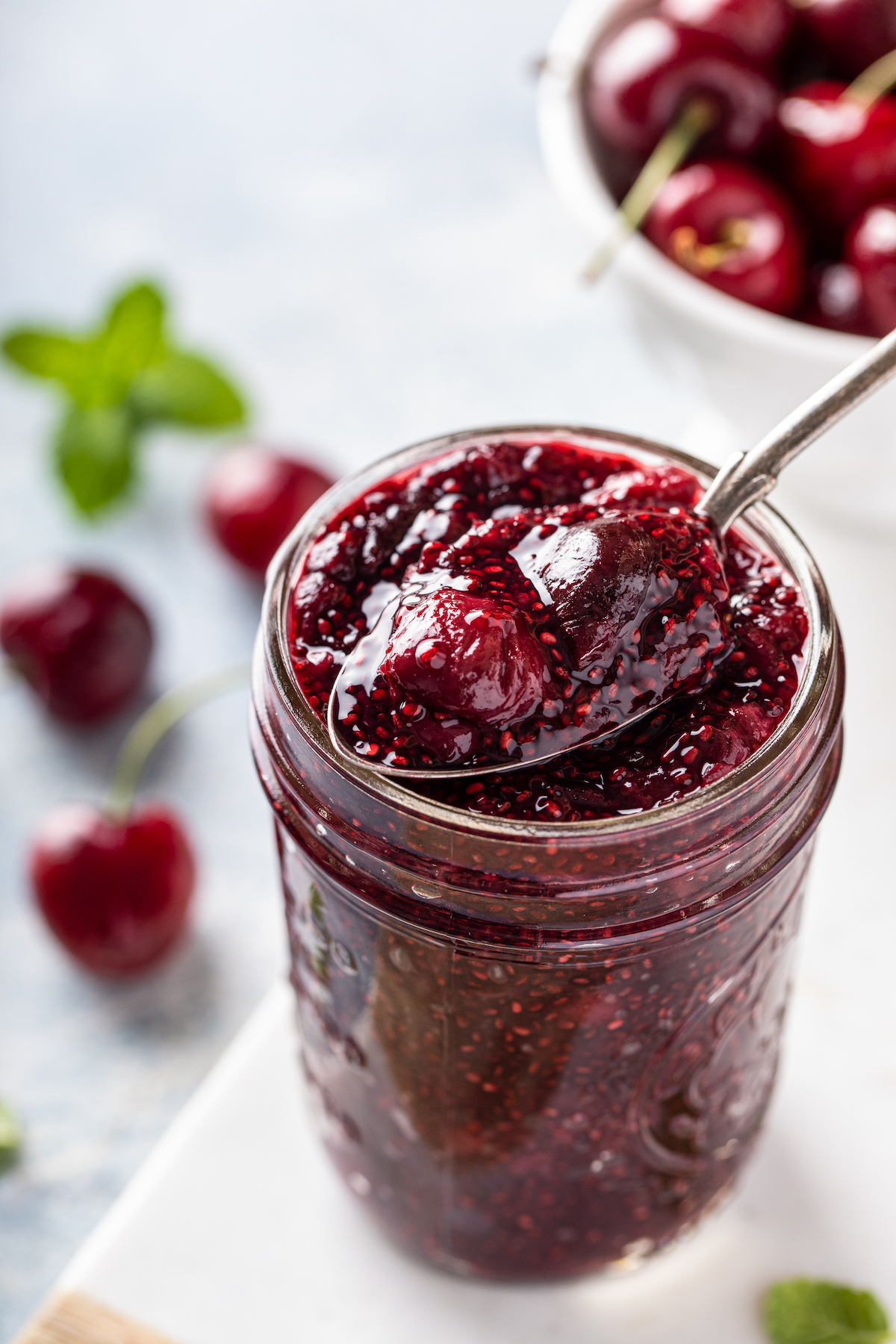 A mason jar filled with cherry chia jam with a metal spoon scooping it out.