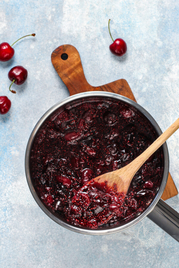 A sauce pan filled with chia cherry jam with cherries scattered around.