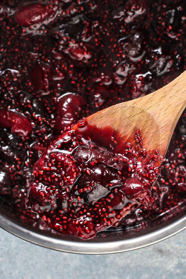 A wooden spoon filled with cherry chia jam.