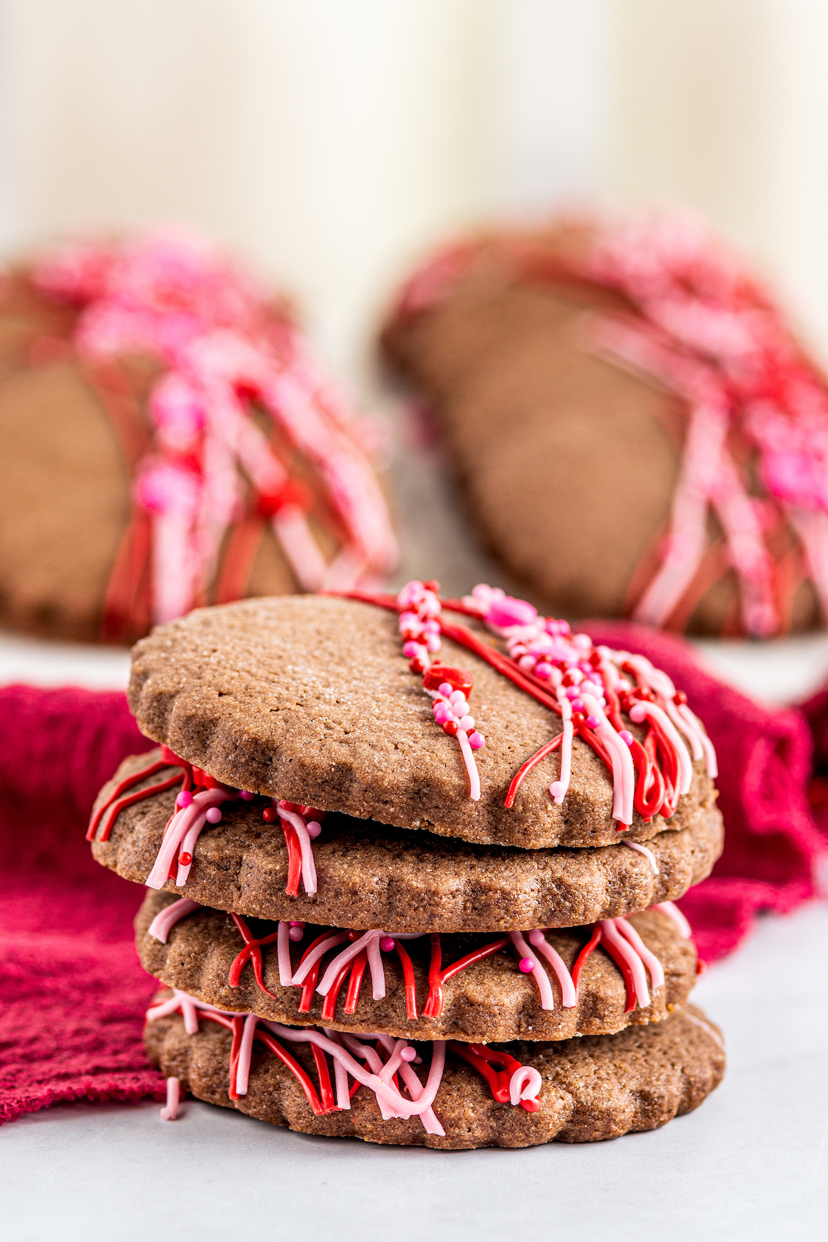 A side view of decorated chocolate cookies, stacked on top of each other. A platter of cookies is in the background of the shot.