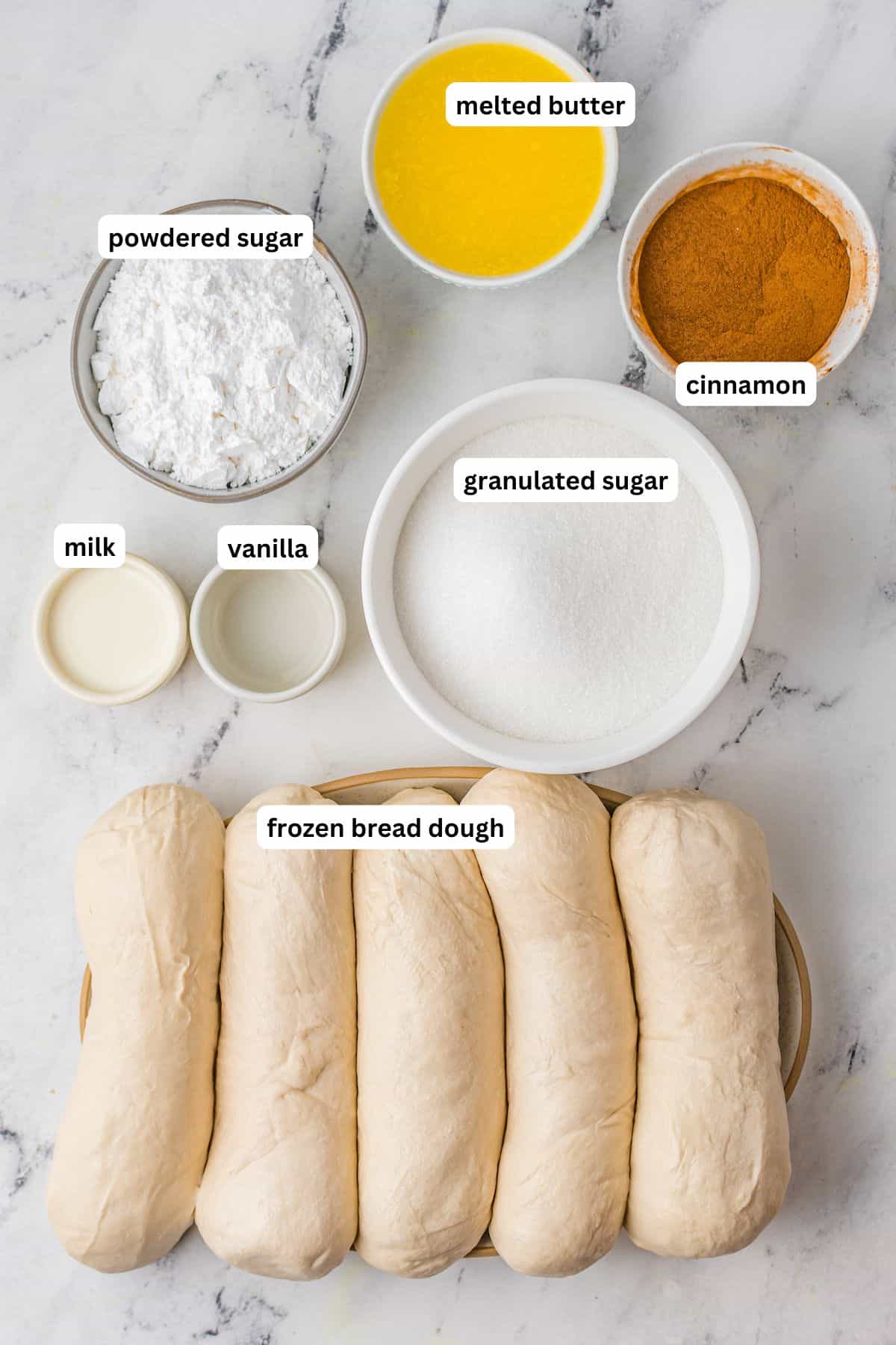 Cinnamon bread ingredients in order from top to bottom: melted butter, powdered sugar, cinnamon, milk, vanilla, granulated sugar, frozen bread dough.