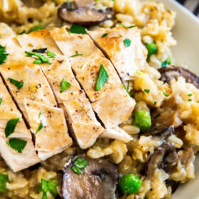 Chicken and rice in a white bowl with mushrooms, peas and parsley on top.