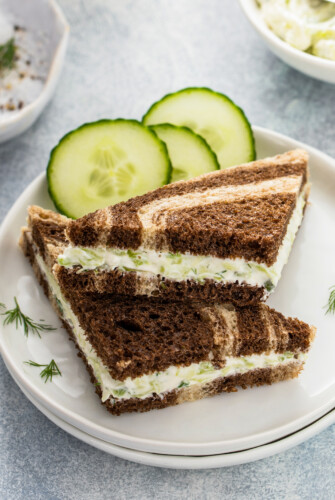 Cucumber sandwiches on a small plate, garnished with slices of cucumber and snipped dill.