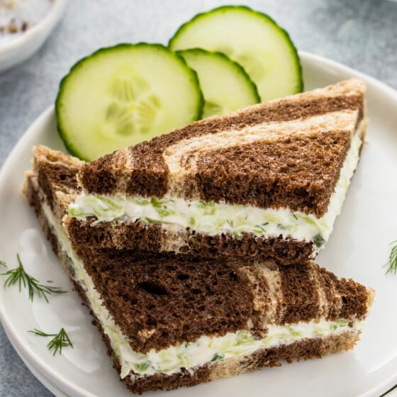 Cucumber sandwiches on a small plate, garnished with slices of cucumber and snipped dill.