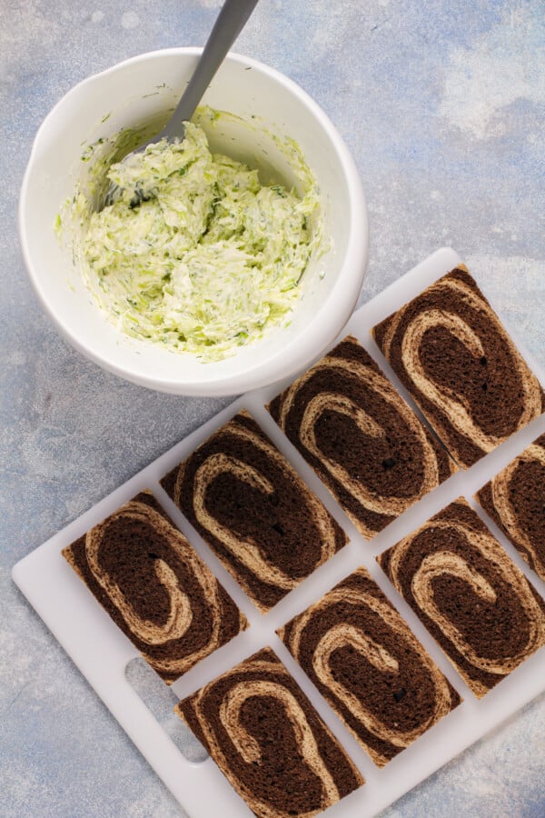 A cutting board with slices of crustless marble rye, next to a bowl of creamy filling.