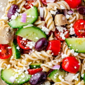 Overhead image of greek pasta salad in a clear glass bowl.