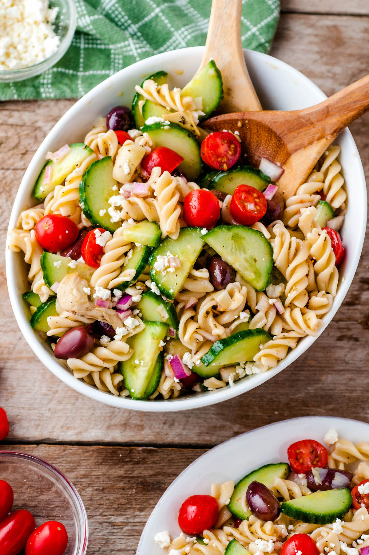 A white bowl with pasta salad with a big wooden spoon.