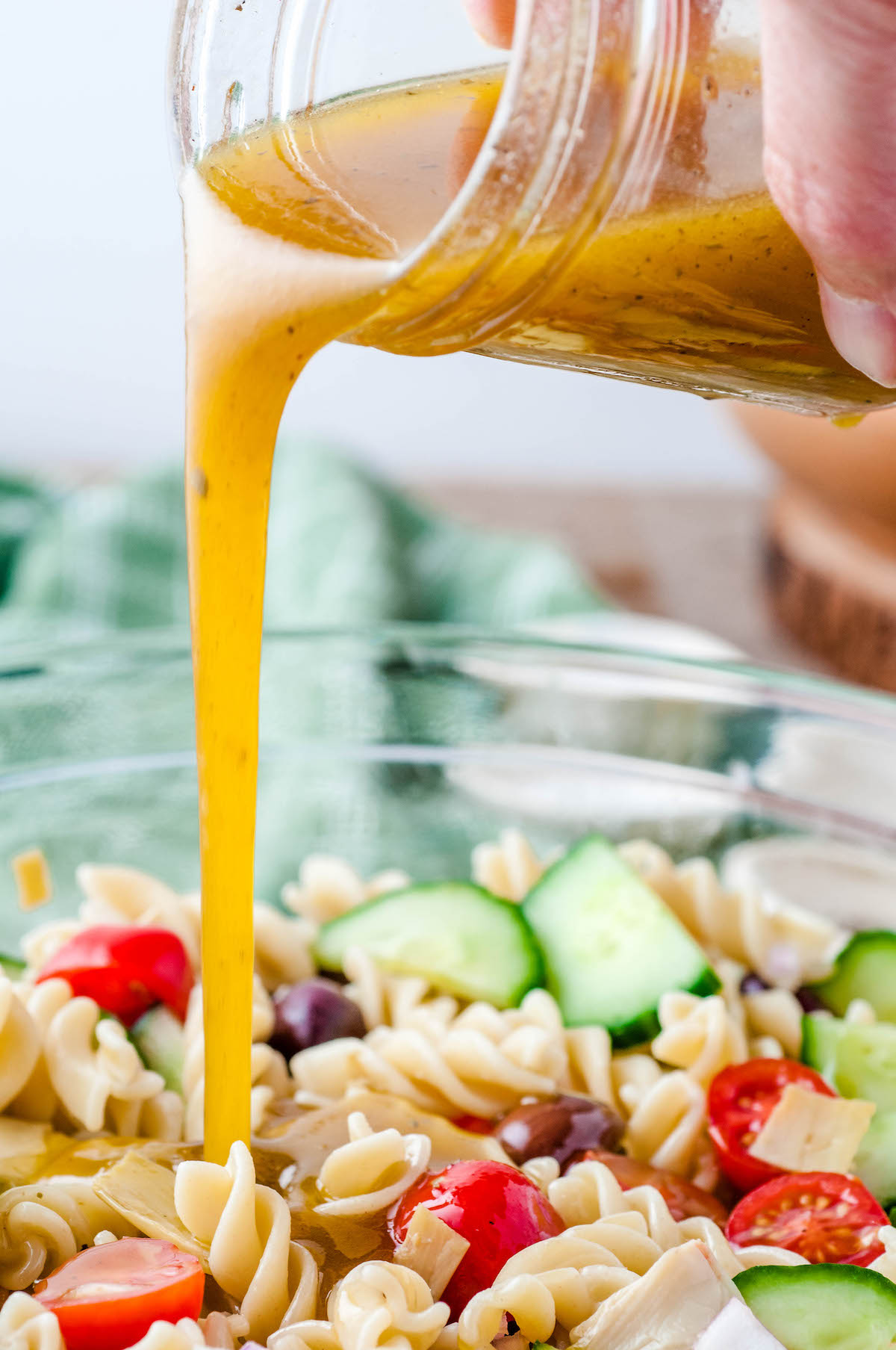 Dressing being poured out of a mason jar and into a bowl of pasta salad.