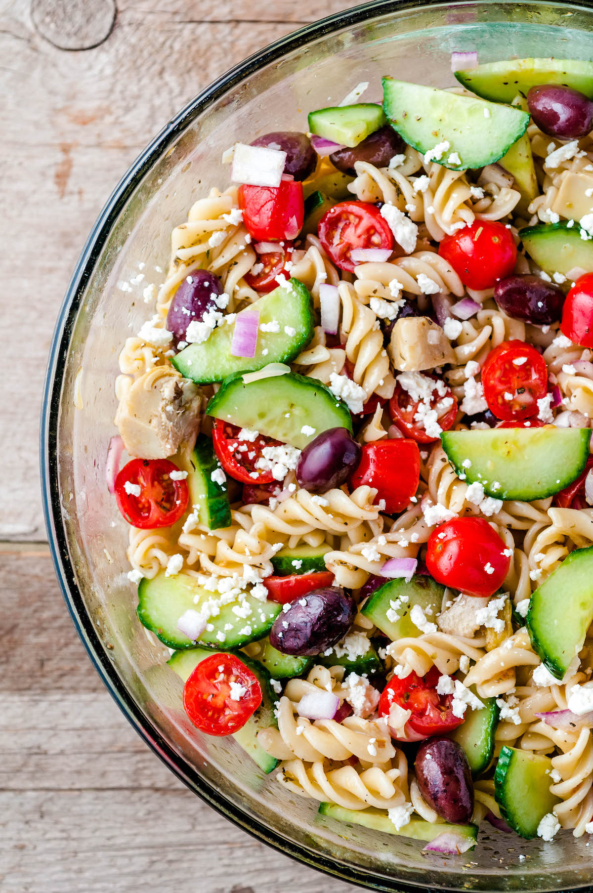 Overhead image of greek pasta salad with feta and olives in a clear glass bowl.