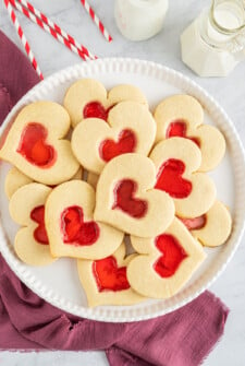 A round white plate with stained glass heart cookies on it.