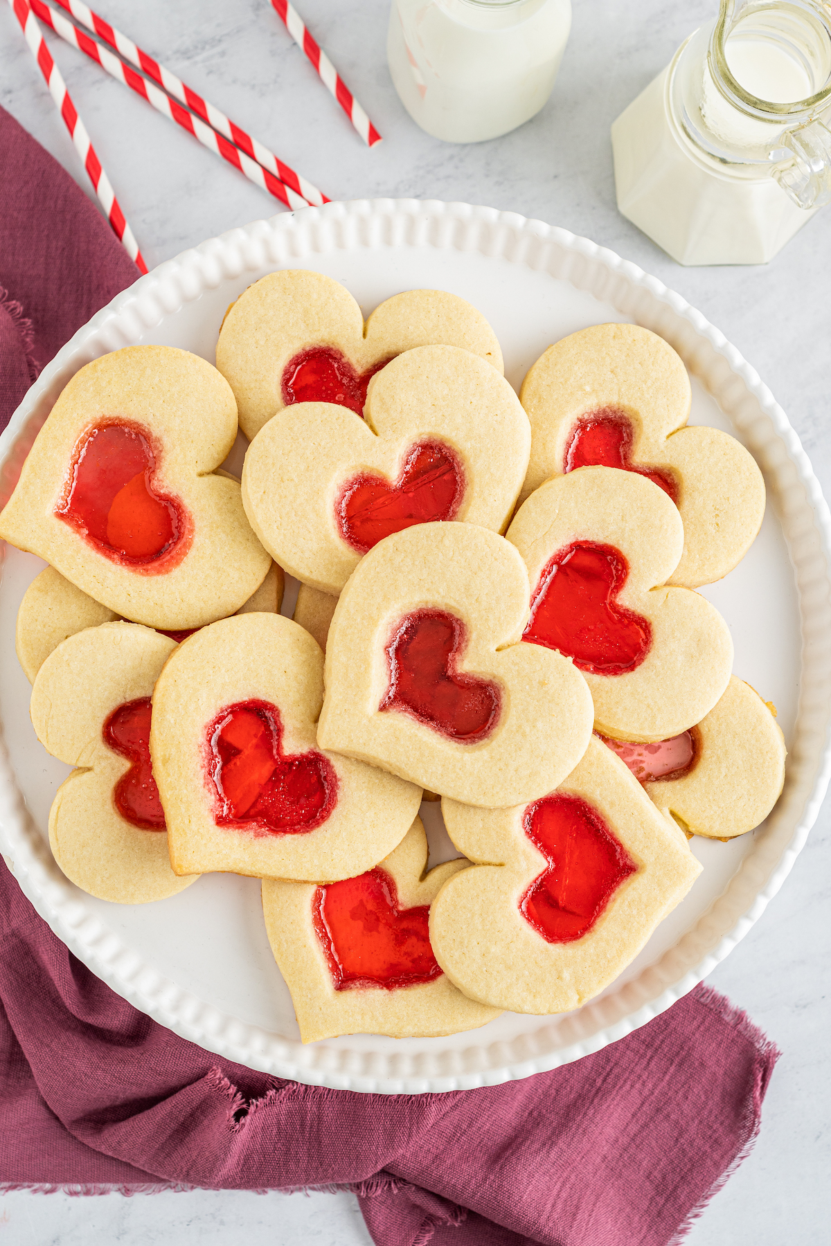 A round white plate with stained glass heart cookies on it.