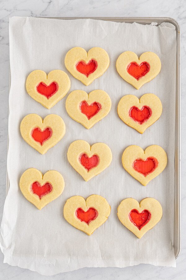 Baked stained glass heart cookies on a parchment-lined baking sheet.