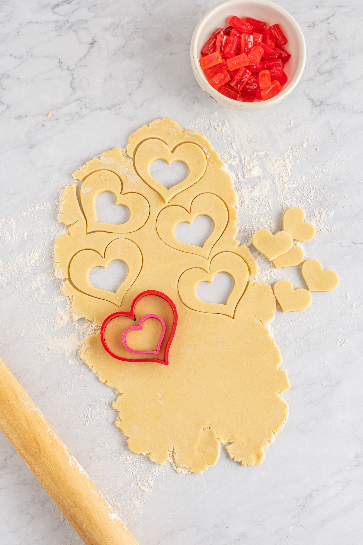 Cookie dough rolled out on a work surface, with heart-shaped cookies cut out of it.