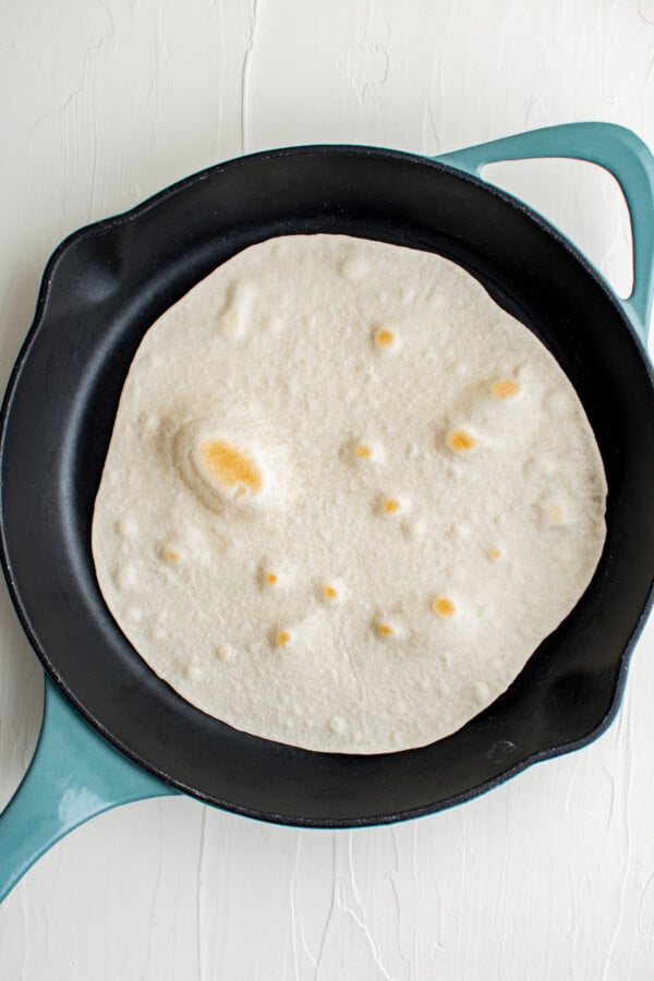 A cast-iron skillet with a tortilla cooking in it. The tortilla is lightly browned on top.