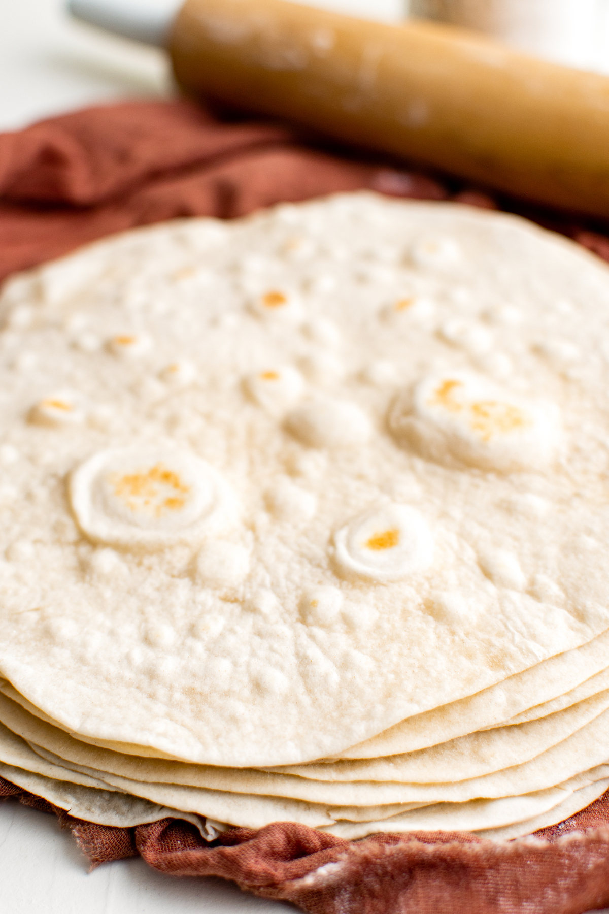 Cooked tortillas in a stack next to a rolling pin and napkin.
