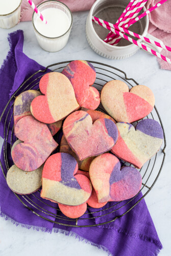 Assorted heart-shaped marbled cookie in a black wire rack on a purple napkin.