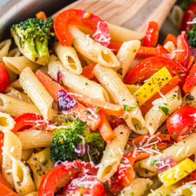 Pasta primavera with pasta, veggies and parmesan cheese on top in a skillet with a wooden spoon.
