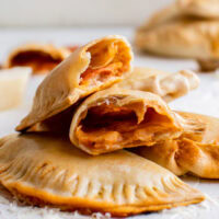 Several empanadas on a work surface. One of the empanadas has been cut in half to show the filling.