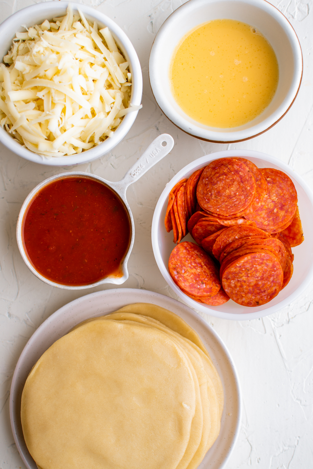 From top left: Shredded mozzarella cheese, egg wash, pizza sauce, pepperoni, and empanada dough.