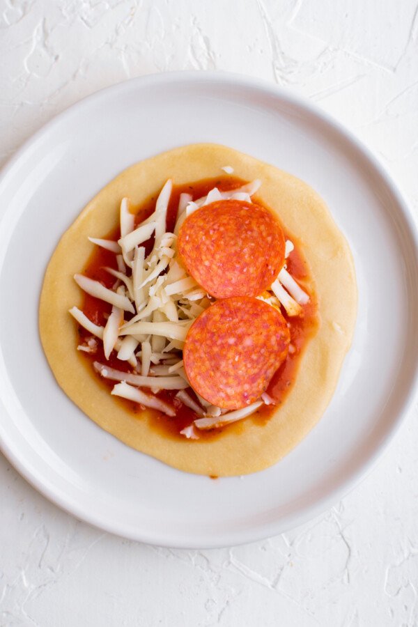 An empanada wrapper topped with sauce, cheese, and pepperoni.