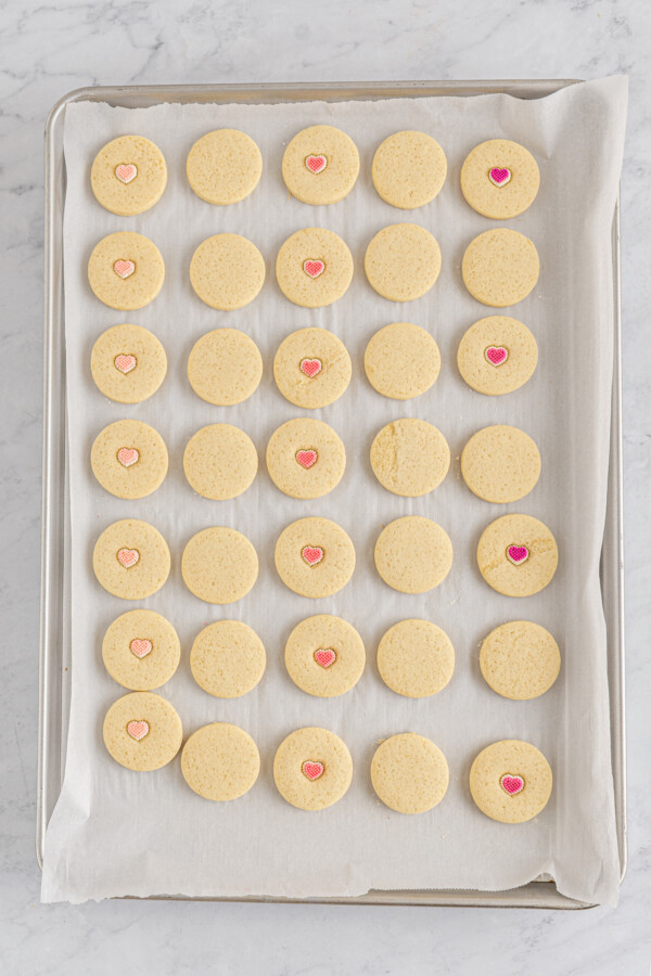 A baking sheet with baked butter cookies on it. Some are decorated with candy hearts, and some are plain.