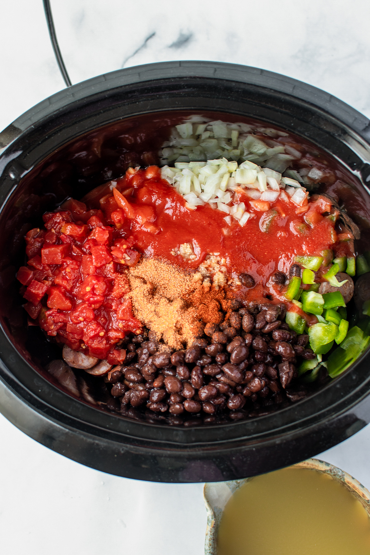 A slow cooker insert with diced tomatoes, tomato sauce, chopped veggies, and black beans added to it.