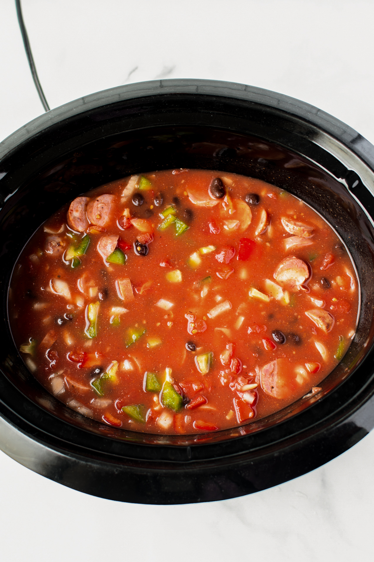 Overhead shot of a crockpot insert filled with veggies, black beans, and other ingredients in a tomato-based sauce.