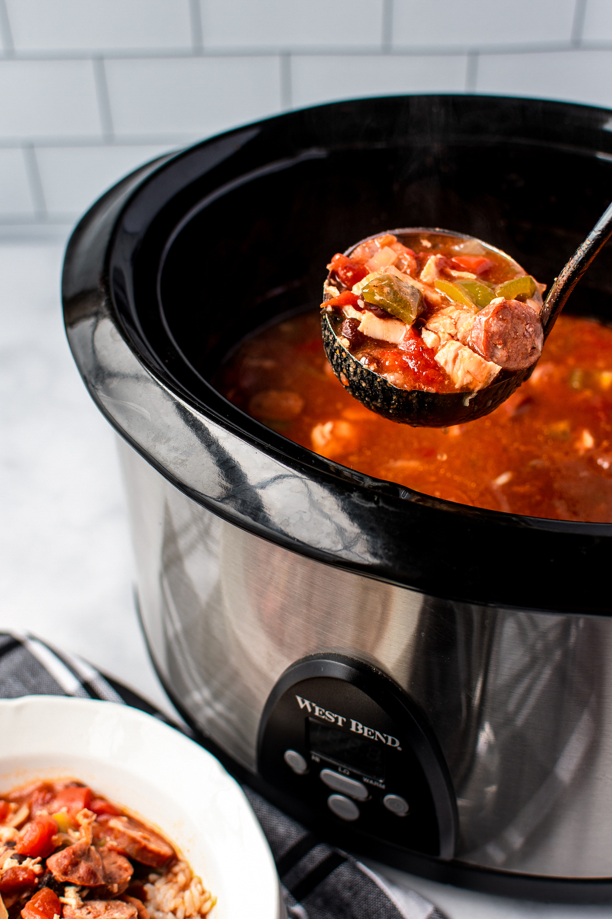 A ladle lifting out chicken, veggies, and sauce from a crockpot.