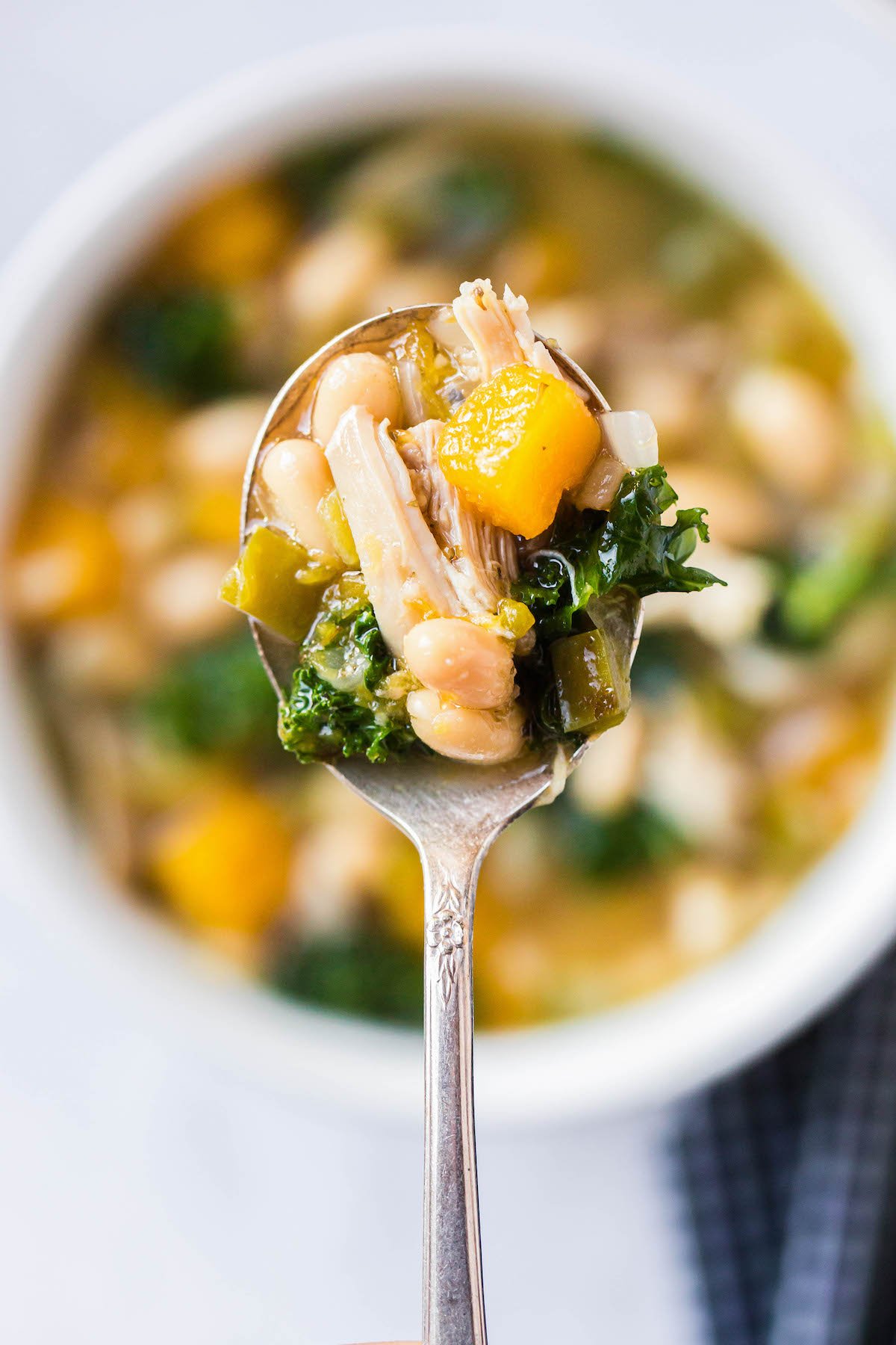 A spoonful of tuscan style chicken soup with kale and butternut squash.