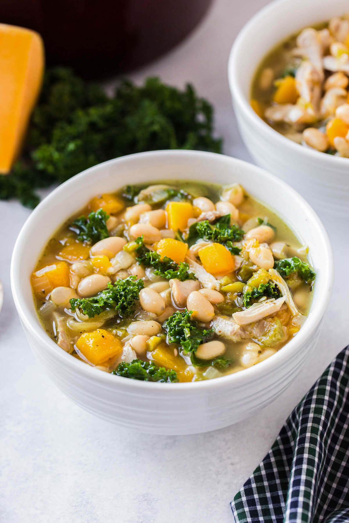 A white bowl filled with tuscan chicken soup with butternut squash, white beans and kale.