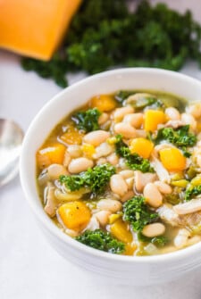 A white bowl filled with chicken and bean soup with kale and butternut squash.