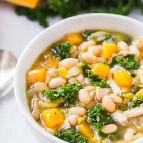 A white bowl filled with chicken and bean soup with kale and butternut squash.