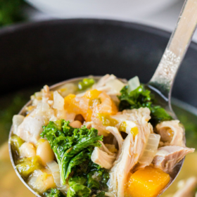 A ladle scooping up a spoonful of tuscan chicken soup with kale.