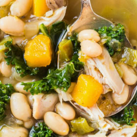 Up close image of a bowl of chicken and vegetable soup in a white bowl with a spoon.